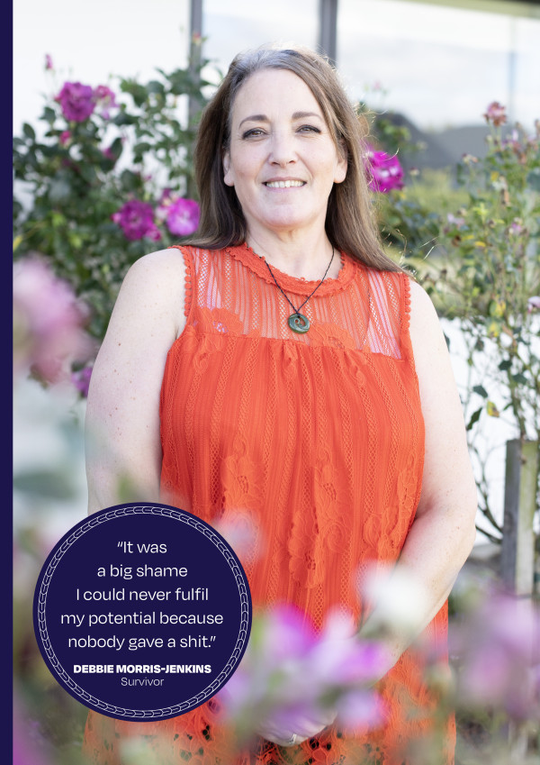 Debbie Morris-Jenkins stands outside in a garden with dark pink rosebushes behind her